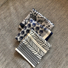 Charger l'image dans la galerie, 3 petits carrés de soie noirs et blancs pliés les uns sur les autres et posés sur un coussin chiné gris