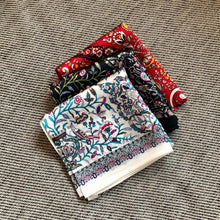 Charger l'image dans la galerie, 3 petits carrés de soir petites fleurs sur fond noir, blanc, ou rouge pliés et posés sur un coussin chiné gris