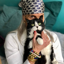 Charger l'image dans la galerie, carré de soie fleurs bleues noué sur la tête d'un femme aux cheveux blancs et tenta dans ses bras un chat noir et blanc