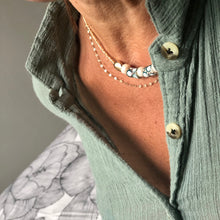 Charger l'image dans la galerie, Collier Cocody avec perle africaine en pâte de verre, perle irisée facettée, perle galet plaqué or sur perles miyuki or, portée sur un cou bronzé et chemise en crèpe de coton kaki clair