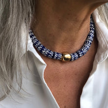 Charger l'image dans la galerie, un collier ras du cou en perles céramiques bleues du Ghana et grosse perle large dorée sur le cou d'une femme aux cheveux longs blanc argenté et chemise blanche