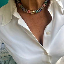 Charger l'image dans la galerie, un collier ras du cou en perles céramiques multicolores du Ghana et grosse perle large dorée sur le cou d'une femme aux cheveux longs blanc argenté et chemise blanche