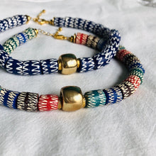 Charger l'image dans la galerie, 2colliers ras du cou en perles céramiques bleues ou multicolores du Ghana et grosse perle large dorée sur un tissu blanc