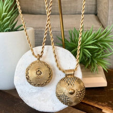 Charger l'image dans la galerie, Gros plan sur 2 sautoirs chaine torsadée dorée et pendentifs ronds africains. Ambiance intérieur bois blanc et plantes grasses
