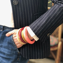 Charger l'image dans la galerie, Bracelets joncs divers en résine style vintage, corail bordeaux et crème sur poignet chemise blanche et veste rayé main dans poche de jean.