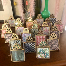 Charger l'image dans la galerie, Accumulation d'une vingtaine de minis cadres à poser en laiton doré. Dans chaque mini cadre il y a des imprimés colorés différents. Ambiance chaleureuse et colorée.