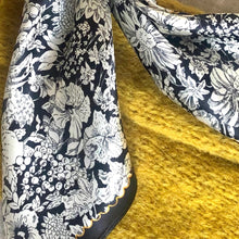 Charger l'image dans la galerie, Gros plan sur un petit carré de soie avec motifs fleurs sur fond noir posé sur une laine tricotée jaune safran