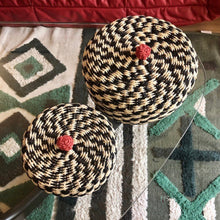 Charger l'image dans la galerie, Gros plan vu du dessus sur panier et son couvercle au pompon rouge en fibre végétale tressée noire et crème.Deux tailles de panier. Ambiance bohème chic.