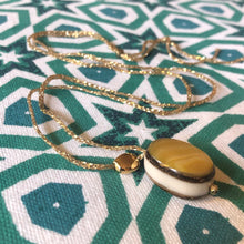 Charger l'image dans la galerie, Gros plan sur sautoir bohème perle nacre forme calisson sur fil d'or présenté sur tissu imprimé étoiles vertes et blanches