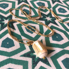 Charger l'image dans la galerie, Gros plan sur sautoir bohème perle nacre forme tube sur fil d'or présenté sur tissu imprimé étoiles vertes et blanches