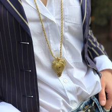 Charger l'image dans la galerie, Plan serré sur sautoir chaine torsadée or avec gros pendentif coeur. Porté sur chemise blanche et veste marine fines rayures. Style ethnique casual