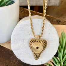 Charger l'image dans la galerie, Gros plan sur pendentif en forme de coeur ajouré en laiton doré sur une chaine torsadée or. Posé sur un rondin de bois peint en blanc.