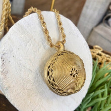 Charger l'image dans la galerie, Gros plan sur pendentif rond avec spirales en laiton doré sur une chaine torsadée or. Posé sur un rondin de bois peint en blanc.