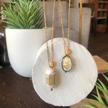 Charger l'image dans la galerie, Présentation de 2 sautoirs bohème avec perles en nacre, perle galet plaqué or le tout sur fil d'or. Ambiance douce bois blanc et plantes grasses.