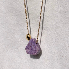 Charger l'image dans la galerie, Sautoir talisman bohème composé d'une perle améthyste forme triangle et d'une perle galet plaqué or sur fil doré. Fond blanc.