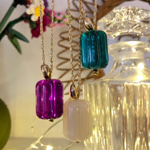 Charger l'image dans la galerie, 3 grosses perles pendentif cannelé en résine crème, framboise et émeraude et perle galet plaquée or sur un fil d'or d'un sautoir bohème réglable sur fond flou ambiance lumineuse et glamour