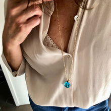 Charger l'image dans la galerie, Sautoir talisman bohème sur fil d'or avec perle pendentif en verre aqua et perle galet plaquée or sur décolleté chemise blanche