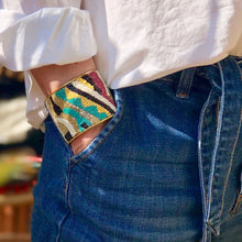 Charger l'image dans la galerie, Bracelet manchette perlée motif couleurs et laiton doré portée par une femme blonde chemise blanche et jean mains dans la poche