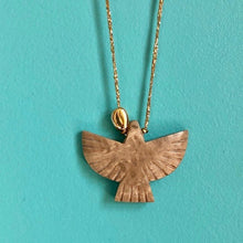 Charger l'image dans la galerie, Gros plan sur sautoir talisman bohème avec perle forme aigle en pierre écaille de tortue et galet doré à l'or fin sur fil doré. Fond bleu turquoise.