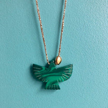 Charger l'image dans la galerie, Gros plan sur sautoir talisman bohème avec perle forme aigle en malachite et galet doré à l'or fin sur fil doré. Fond bleu turquoise.