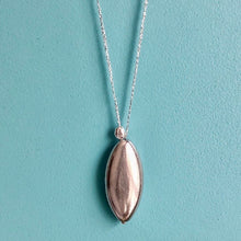 Charger l'image dans la galerie, Gros plan sur sautoir talisman bohème avec grosse perle forme ellipse en résine galvanisée argentée et galet plaqué argent sur fil argent. Fond bleu turquoise.