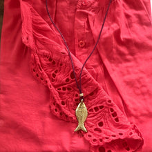 Charger l&#39;image dans la galerie, Collier sautoir pendentif poisson en laiton doré sur lien de cuir présenté sur une chemise dentelle en coton corail
