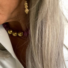 Charger l&#39;image dans la galerie, Gros plan sur une boucle d&#39;oreille or en forme de losange d&#39;inspiration byzantine sur femme aux cheveux blanc argent  en chemise blanche.
