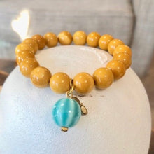 Charger l&#39;image dans la galerie, Gros plan sur un bracelet de grosses perles en Jaspe Mokaite poli jaune indien associées à une perle pampille en céramique bleue clair légèrement rayée . Ambiance épurée

