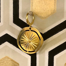 Charger l&#39;image dans la galerie, Gros plan sur une boucle d&#39;oreille forme médaille soleil contemporain sur un papier peint de forme géométrique noir, blanc, beige et or
