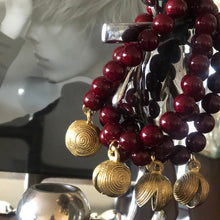 Charger l&#39;image dans la galerie, Mise en scène de plusieurs bracelets en perles rondes bordeaux et breloque d&#39; Afrique en laiton doré 
