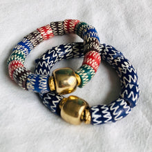 Charger l&#39;image dans la galerie, 2 bracelets en perles céramiques bleues ou multicolores du Ghana et grosse perle large dorée sur un tissu blanc
