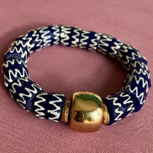 Charger l&#39;image dans la galerie,   bracelet en perles céramiques bleues du Ghana et grosse perle large dorée sur un tissu rose
