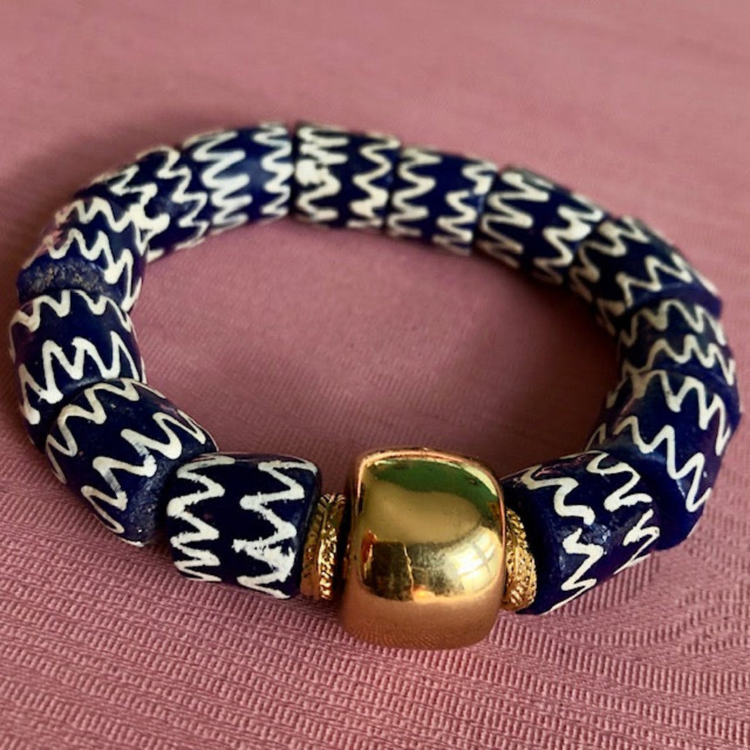   bracelet en perles céramiques bleues du Ghana et grosse perle large dorée sur un tissu rose