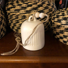 Charger l&#39;image dans la galerie, Cloche en céramique blanche et son système d&#39;accroche en ficelle et perles en bois brut.Posée sur meuble en bois foncé.
