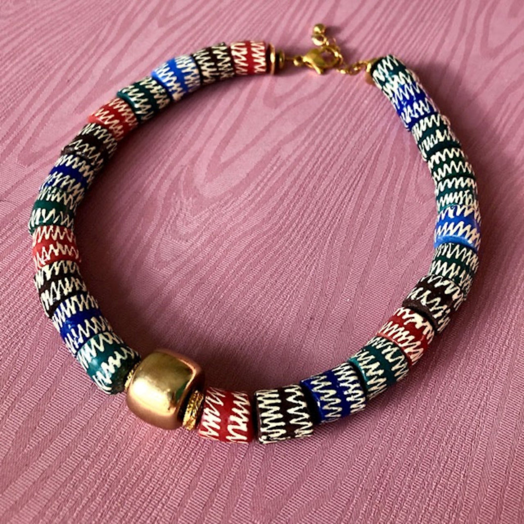 un collier ras du cou en perles céramiques multicolores du Ghana et grosse perle large dorée sur un fond de tissu rose