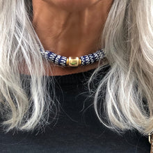 Charger l&#39;image dans la galerie, un collier ras du cou en perles céramiques bleues du Ghana et grosse perle large dorée sur le cou d&#39;une femme aux cheveux longs blanc argenté et pull noir
