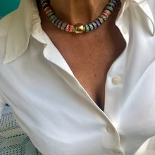 Charger l&#39;image dans la galerie, un collier ras du cou en perles céramiques multicolores du Ghana et grosse perle large dorée sur le cou d&#39;une femme aux cheveux longs blanc argenté et chemise blanche

