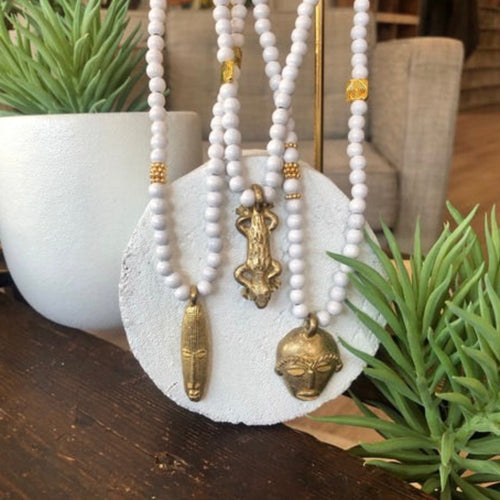 Gros plan de 3 sautoirs de perles de bois blanc et pendentifs africains en laiton doré. Ambiance d'un salon bois et plantes grasses