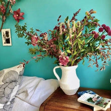 Charger l&#39;image dans la galerie, Vase cruche brut et blanc avec un gros bouquet de fleurs des champs multicolores sur table de nuit avec livres et sur fond d&#39;un mur turquoise
