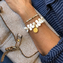 Charger l&#39;image dans la galerie, Bracelet en perles de nacre blanche et forme de goutte à coté d&#39;un bracelet surfeur nacre et miyuki or sur poignet bronzé tenant un sac blanc et chemise bleue
