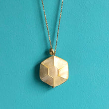 Charger l&#39;image dans la galerie, Gros plan sur sautoir talisman bohème avec grosse perle hexagonale en nacre et galet doré à l&#39;or fin sur fil doré. Fond bleu turquoise.

